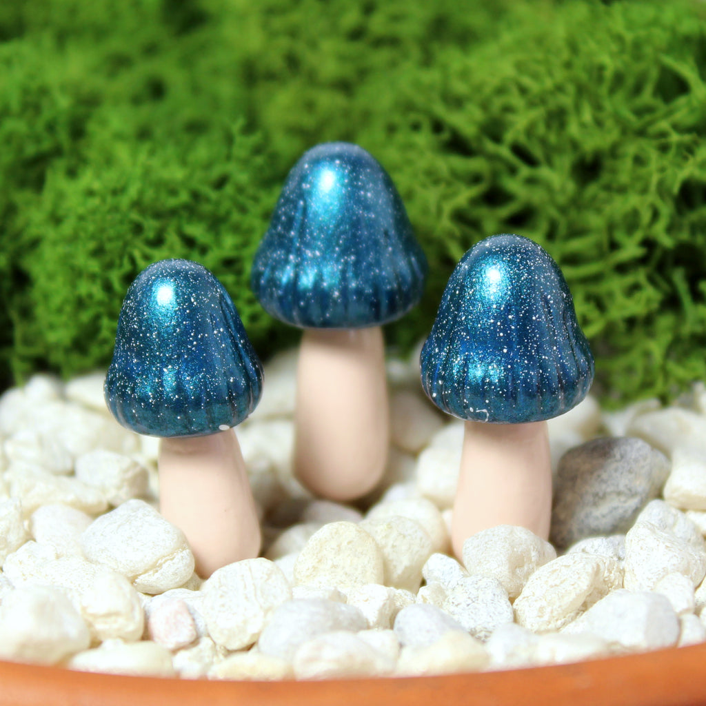 Three sparkly indigo blue fairy mushrooms sit in a moss garden with white gravel