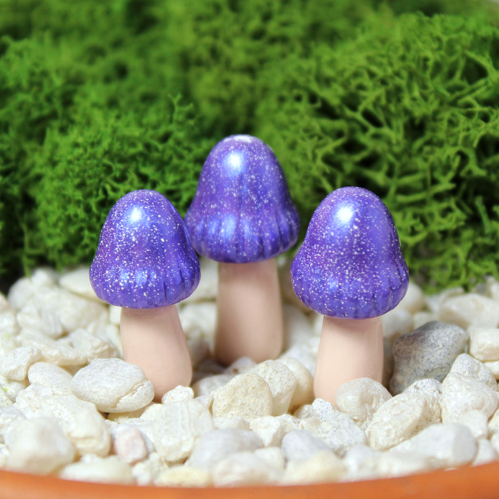 Three sparkly royal purple fairy mushrooms sit in a moss garden with white gravel