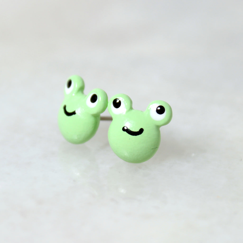 A pair of green frog earrings rest on top of a marble surface